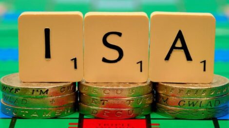 Scrabble letters spelling out the word "ISA" sitting on three-pound coins.